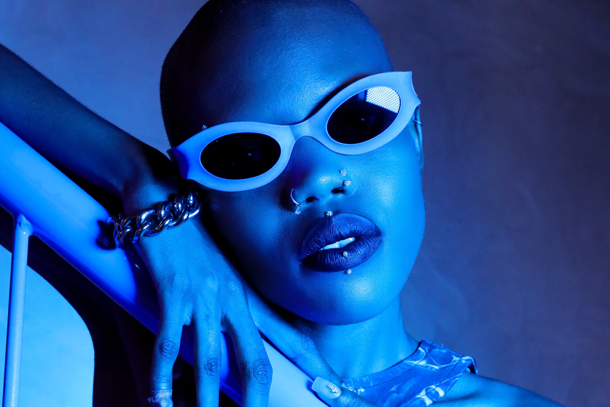 Model wearing REFRAMD Afronaut Oracle parametric sunglasses in blue studio lighting